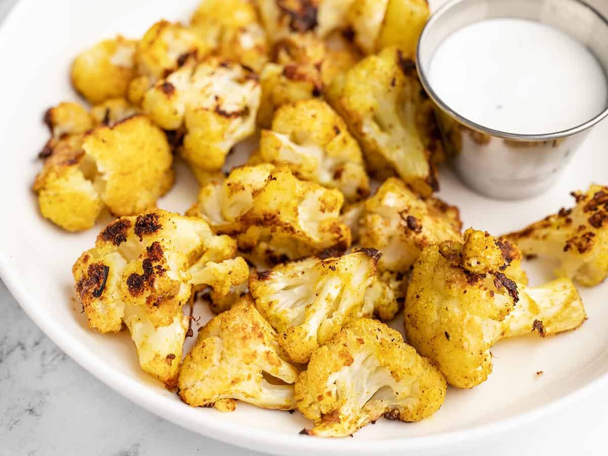 Close up side view of a plate full of curry roasted cauliflower and dipping sauce.