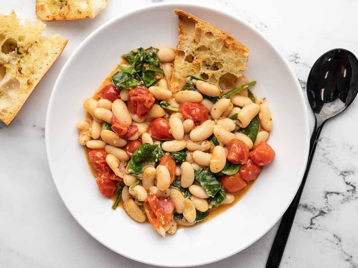 Overhead view of a bowl of saucy white beans with garlic bread on the side. 