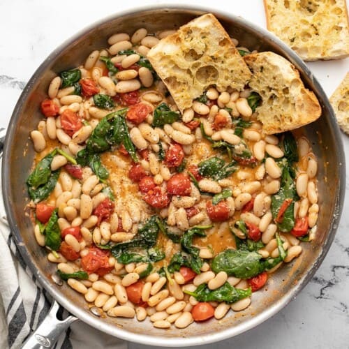 Finished white beans in the skillet with garlic bread in the side.