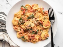 Overhead view of a bowl full of spinach tortellini with a fork in the side.