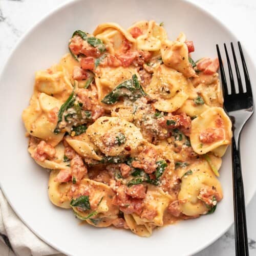 Overhead view of a bowl full of spinach tortellini with a fork in the side.