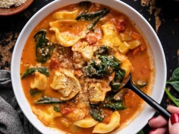 Overhead view of a bowl full of tortellini soup with a spoon lifting a bite.