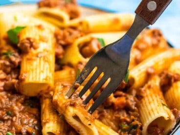 close up side view of lentil bolognese on a plate of rigatoni being pierced with a fork.