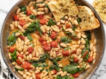 Overhead view of a skillet full of saucy white beans with garlic bread on the side.