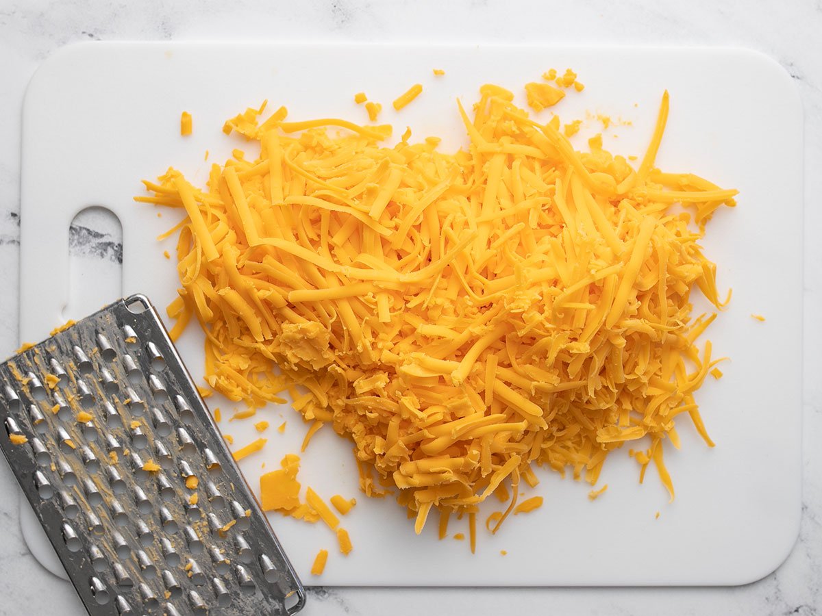Shredded cheddar cheese on a cutting board with the cheese grater. 