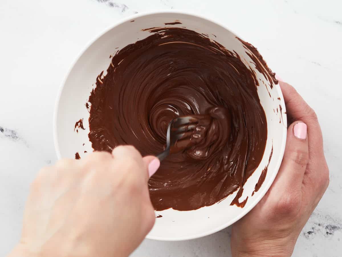 Overhead shot of milk chocolate being melted and stirred in a white bowl.