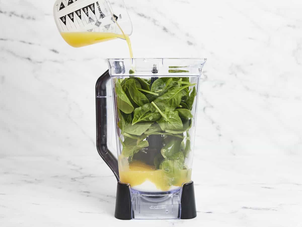 Side shot of juice being added to a blender full of spinach.