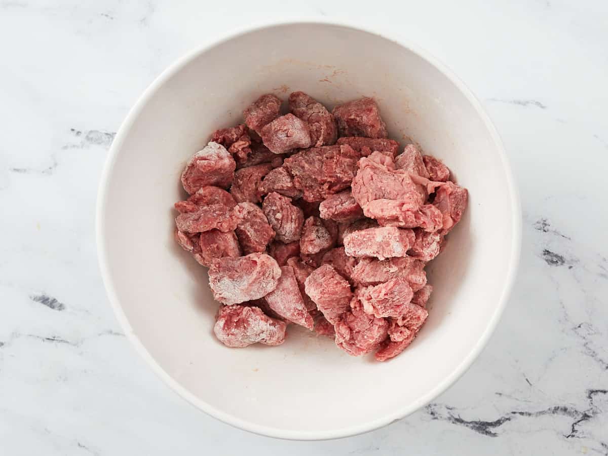 Stew meat in a bowl coated with flour, salt, and pepper.