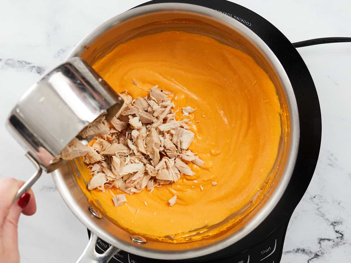 Chopped chicken being poured into the creamy sauce.