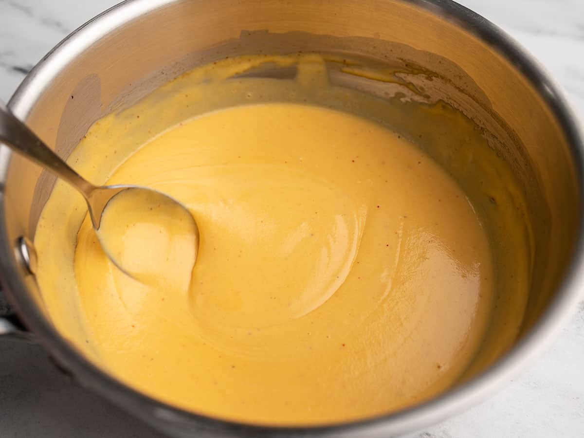 Finished nacho cheese sauce being stirred with a spoon. 