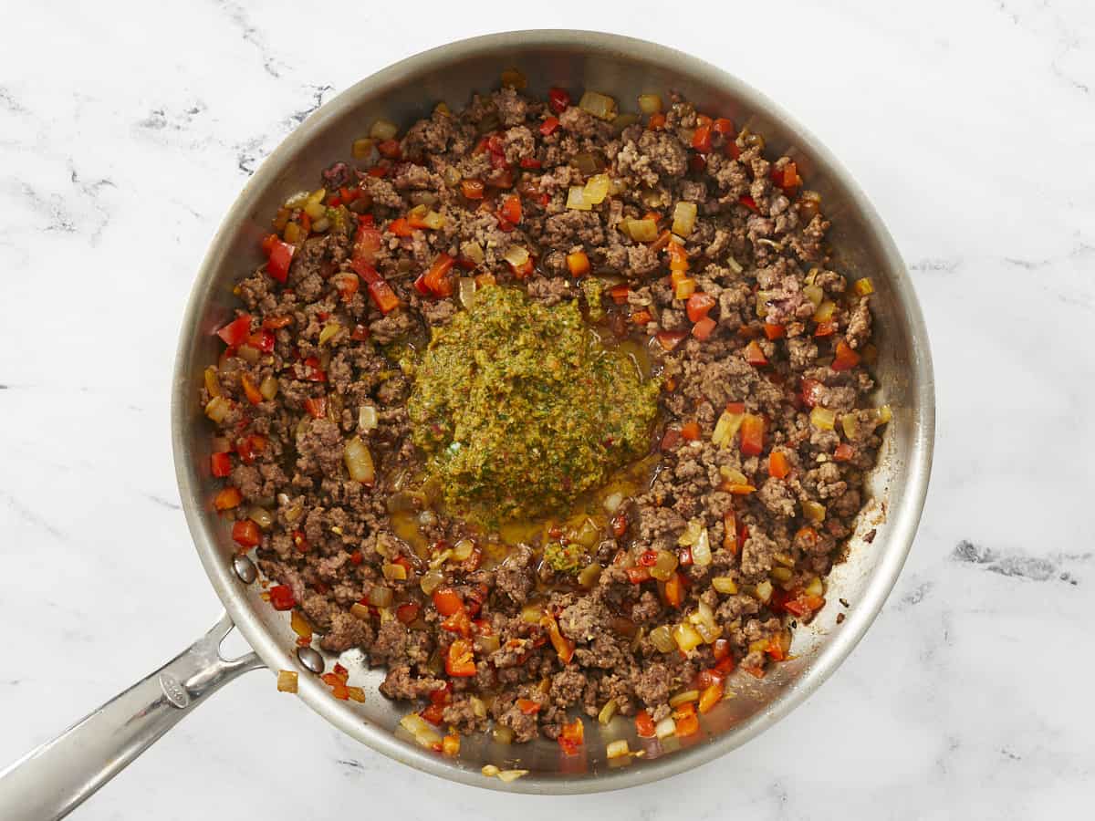 Sofrito being added to a pan with browned meat in it.