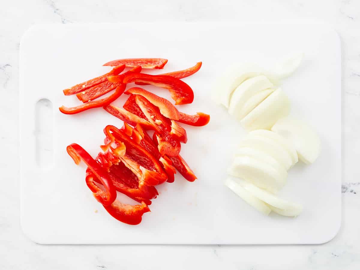 Sliced bell pepper and yellow onion on a cutting board.