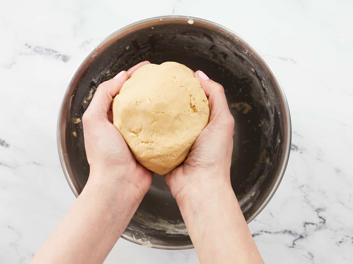 Overhead shot ofof two hands holding a ball of dough over a bowl.