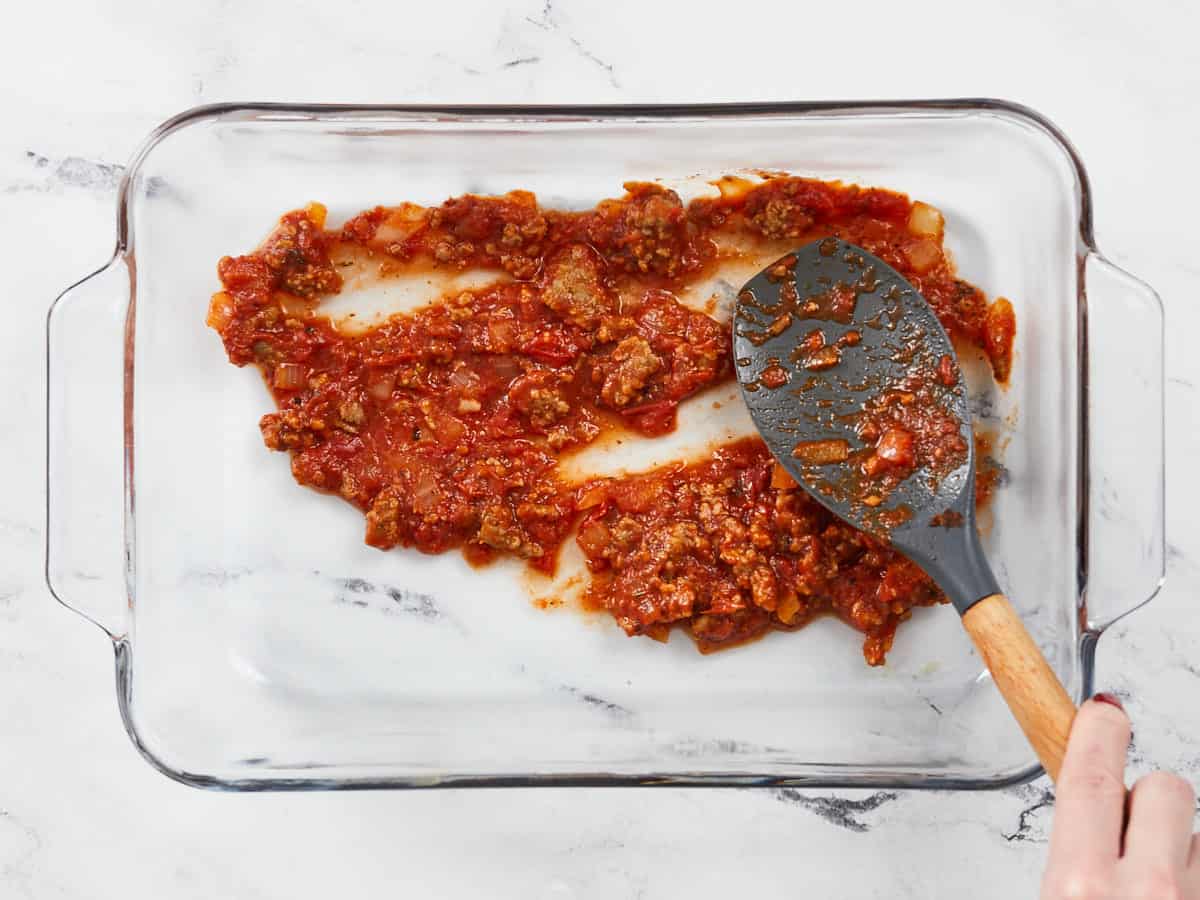 Sauce being spread in a casserole dish.