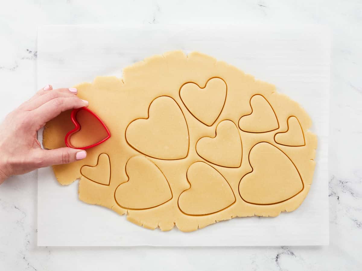 Overhead shot of dough being cut with a heart-shaped cookie cutter.