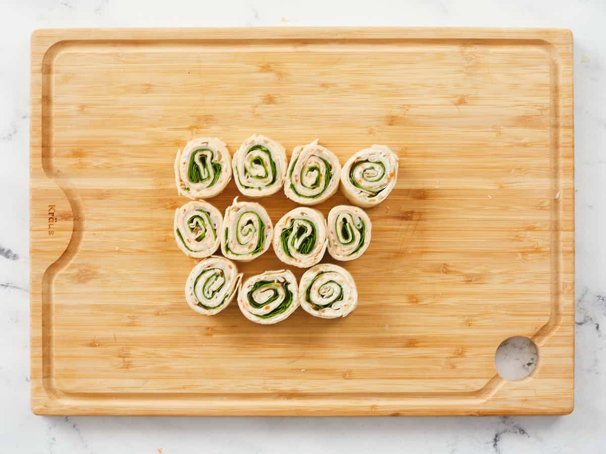 Eleven turkey pinwheels arranged on a wooden cutting board.