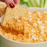 Side view of a cracker being dipped into a bowl of buffalo chicken dip.