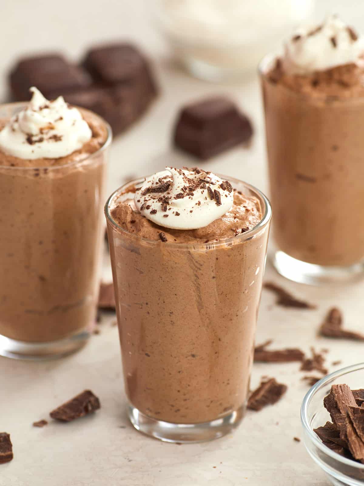 Three cups full of chocolate mousse with whipped cream.