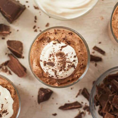 Overhead view of three cups of chocolate mousse with whipped cream and chocolate shavings.