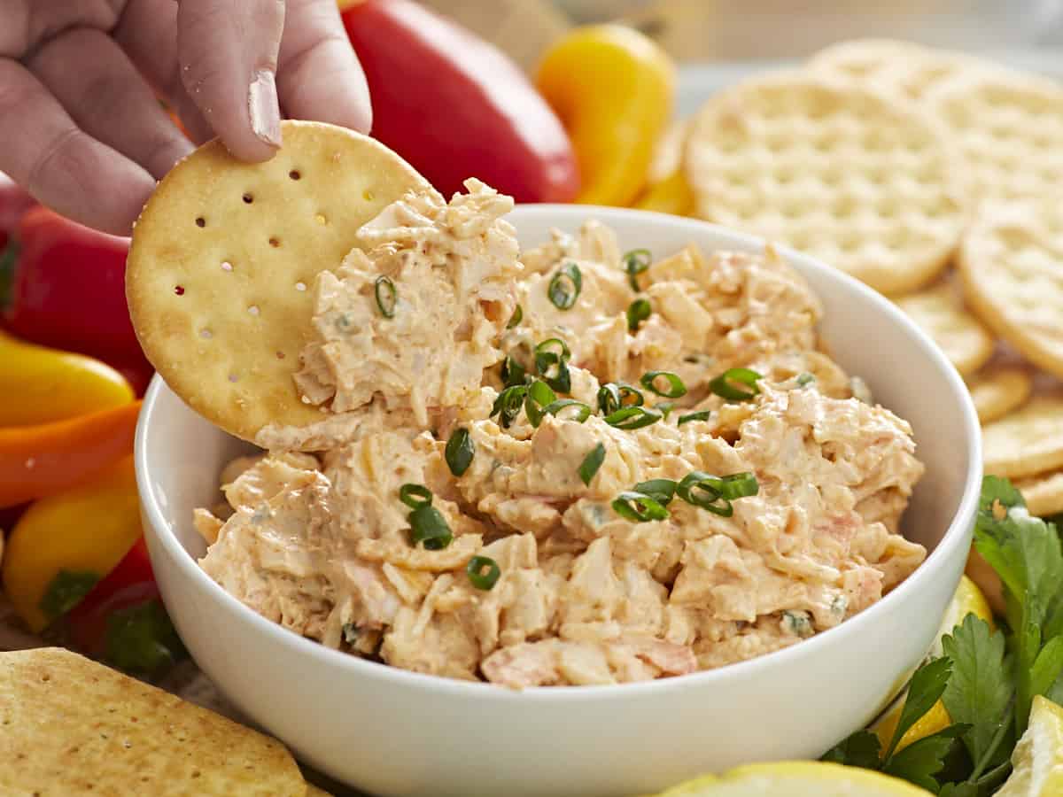 Hand dipping cracker in crab dip.