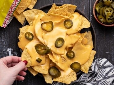 Overhead view of a plate of nachos with a hand stealing one chip.