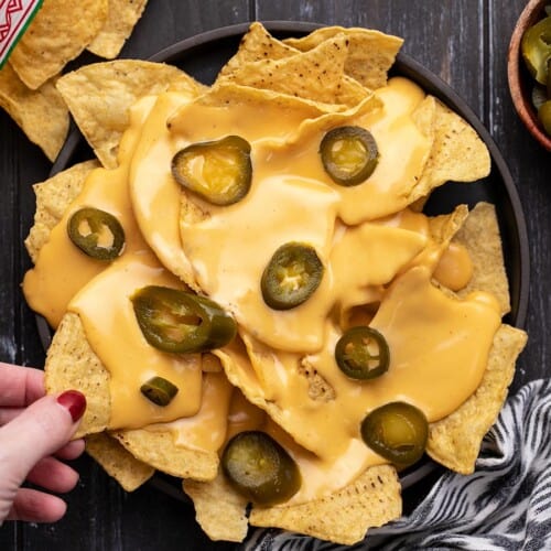 Overhead view of a plate of nachos with a hand stealing one chip.