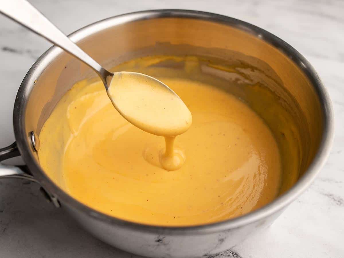 Nacho cheese running off a spoon into a saucepot. 
