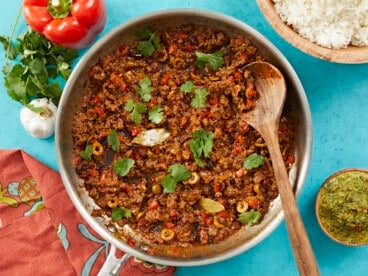 Overhead shot of picadillo in a silver skillet with a wooden spoon in it.