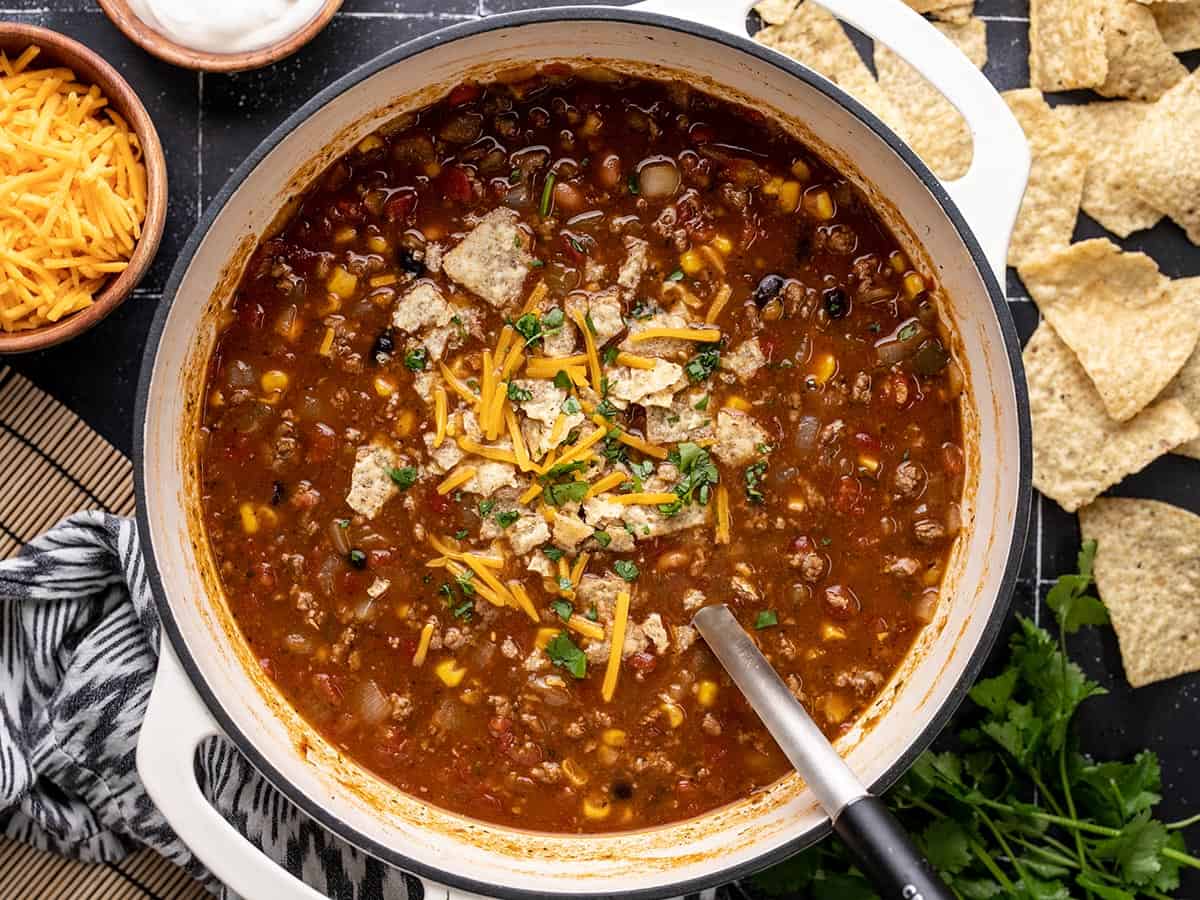 Overhead view of a pot of taco soup with toppings and a ladle.