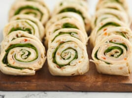 A close up of three rows of turkey pinwheels on a wooden cutting board.