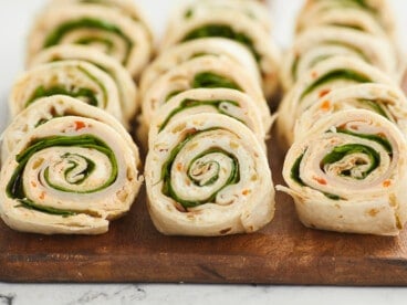 A close up of three rows of turkey pinwheels on a wooden cutting board.
