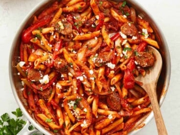 Overhead view of a skillet full of pasta with sausage and peppers, and a wooden spoon.