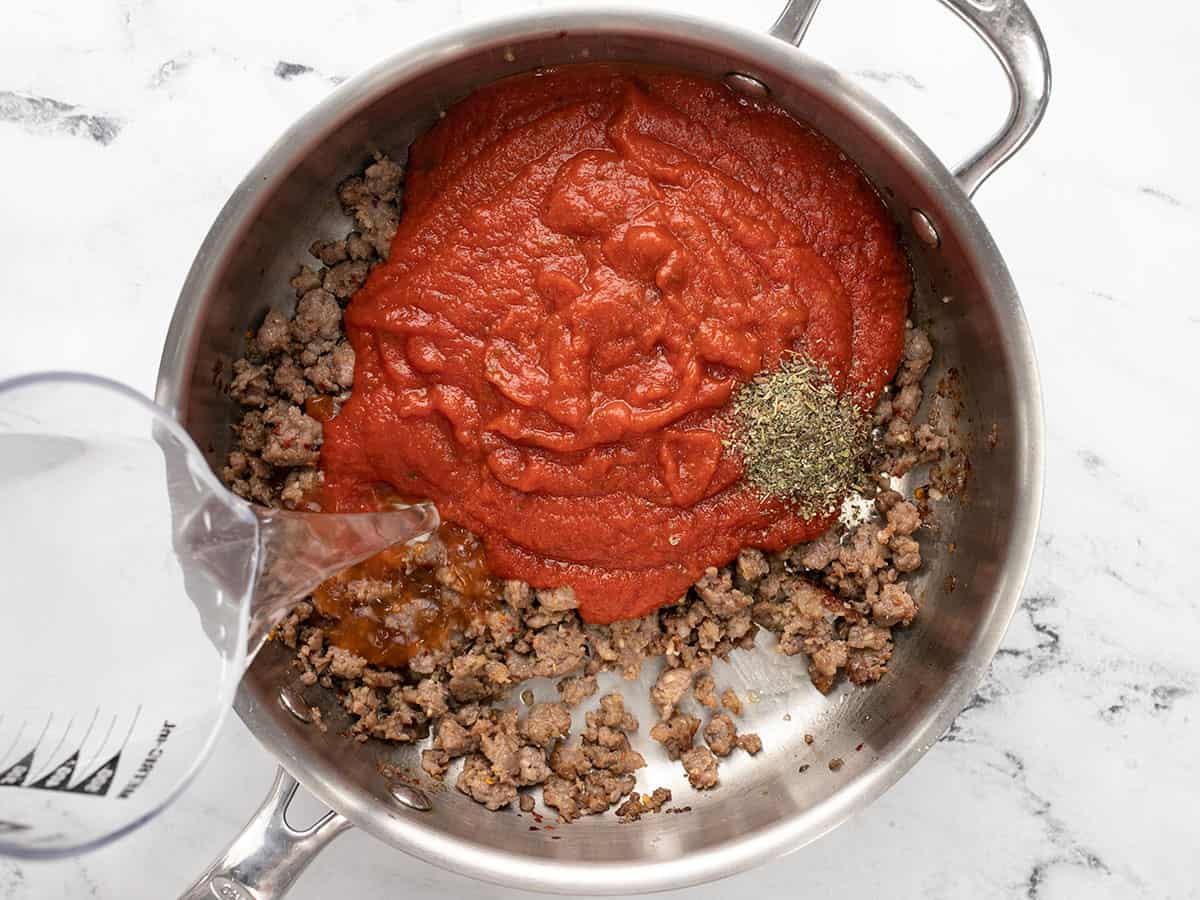 Sauce, herbs, and water added to the skillet.