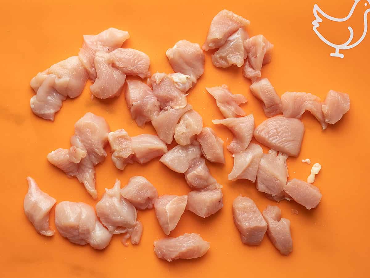 Chicken cut into chunks on an orange cutting board.