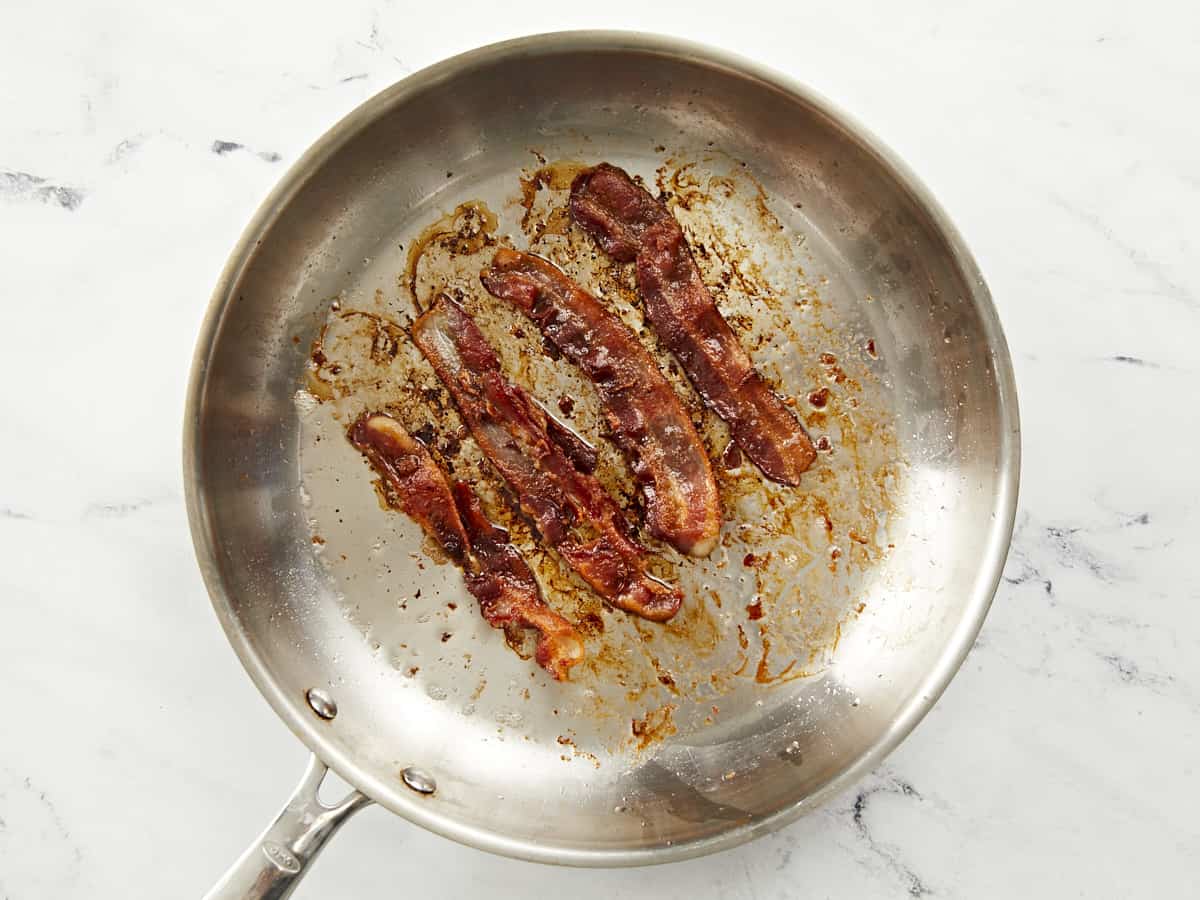 Overhead shot of bacon frying in a pan.