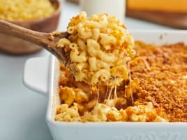 Side view of baked mac and cheese being lifted out of the casserole dish with a wooden spoon.