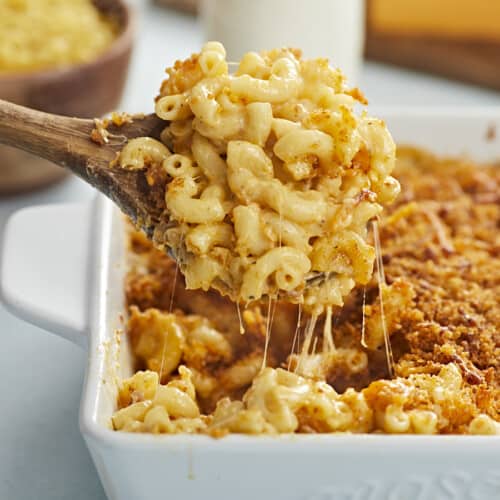 Side view of baked mac and cheese being lifted out of the casserole dish with a wooden spoon.