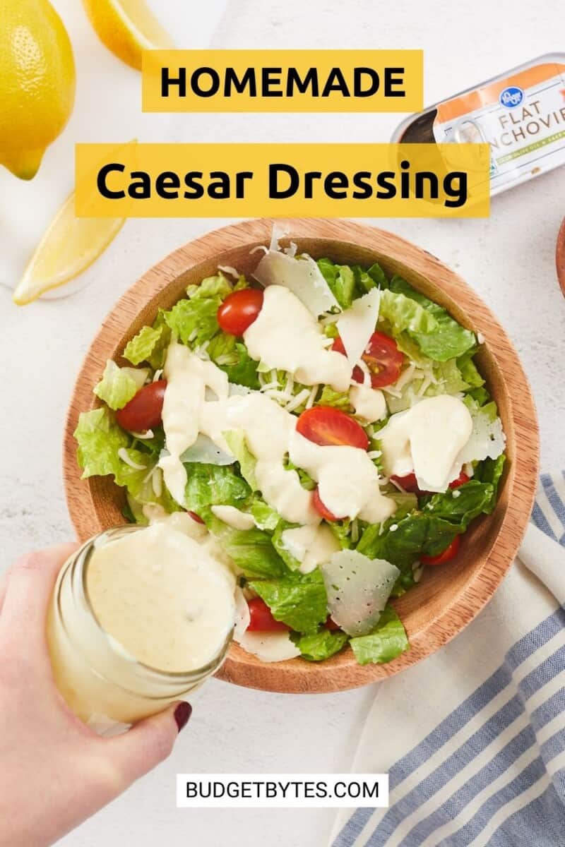 Caesar dressing being poured over a salad in a bowl.