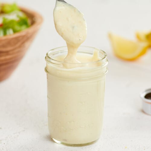 Caesar dressing dripping off a spoon into a jar.