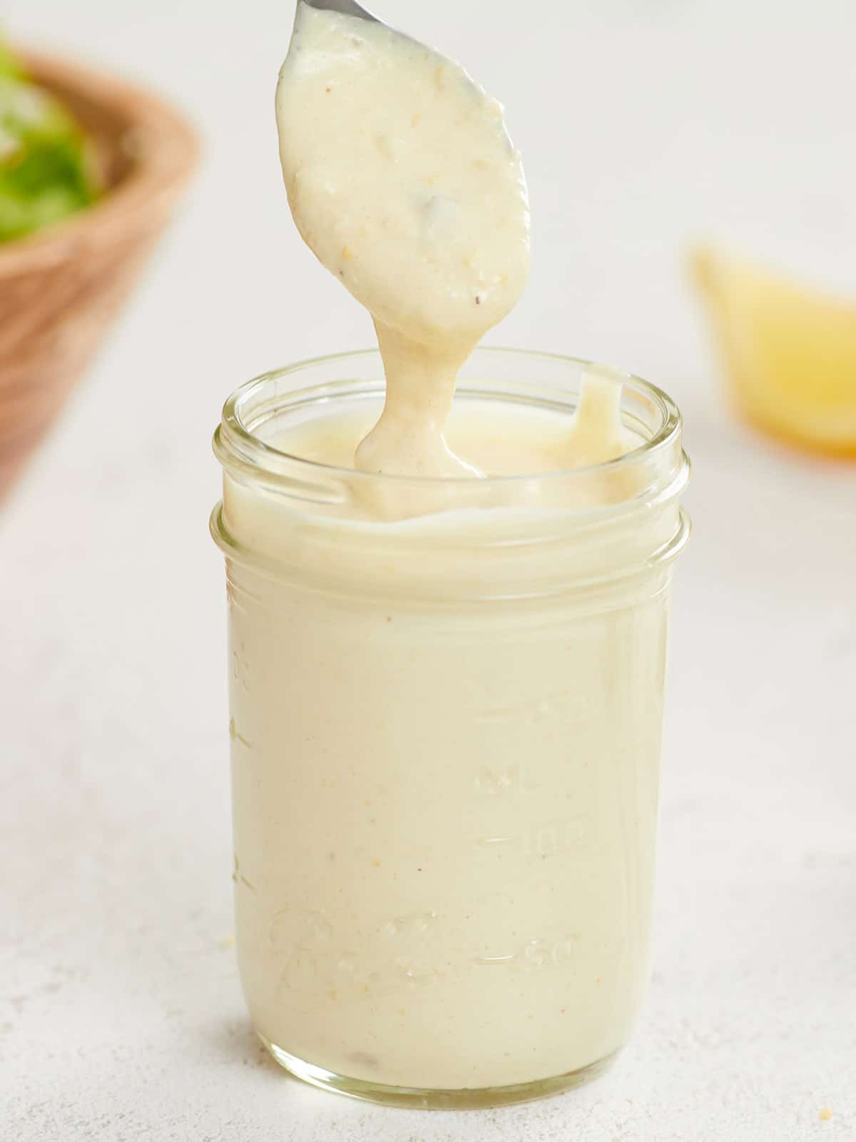 Caesar dressing dripping off a spoon into a jar.