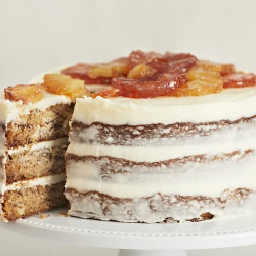 Side shot of Hummingbird Cake with a slice being taken out of it.