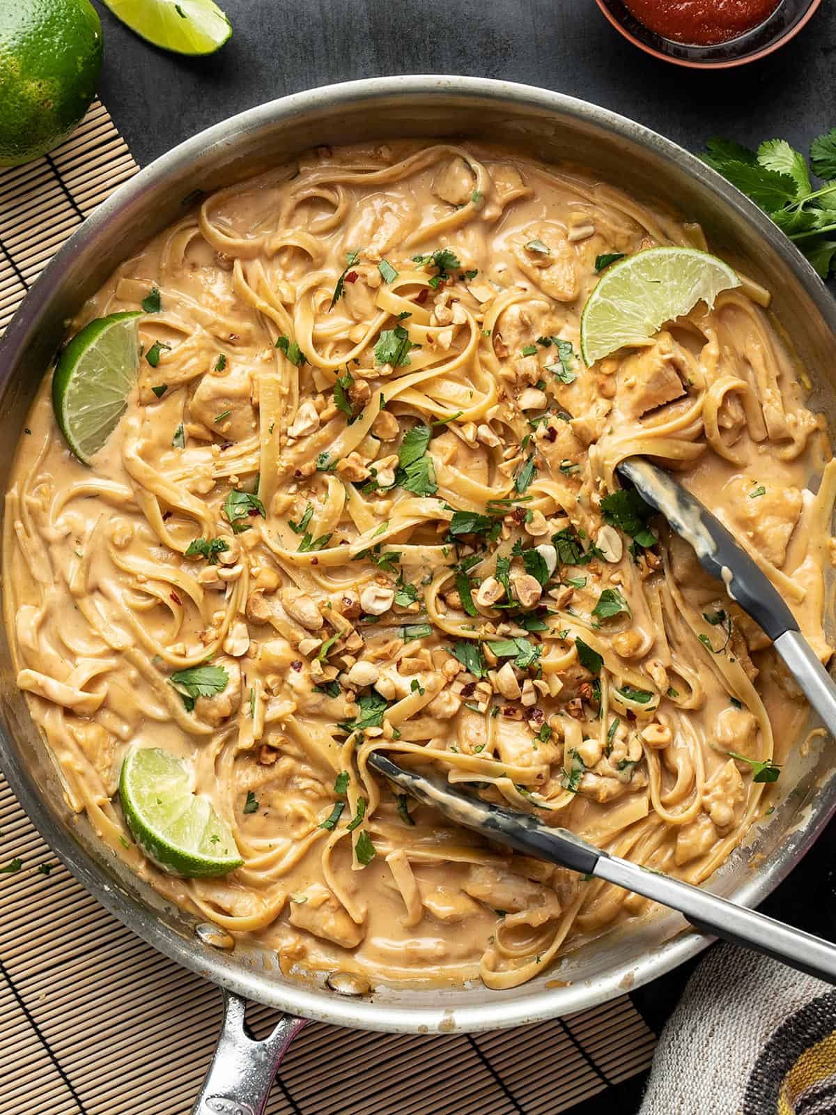 Overhead view of peanut noodles with chicken in a skillet with tongs.