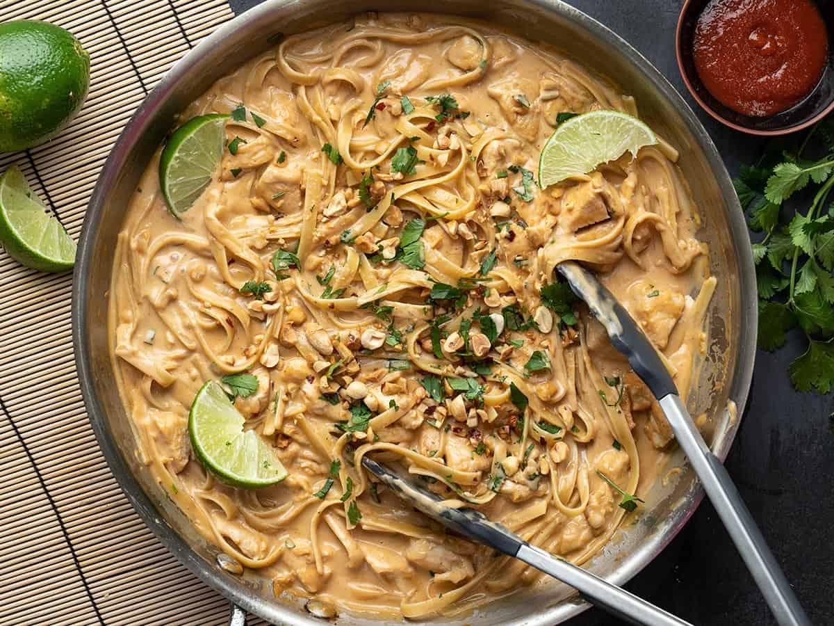 Overhead view of peanut noodles in the skillet with open tongs.