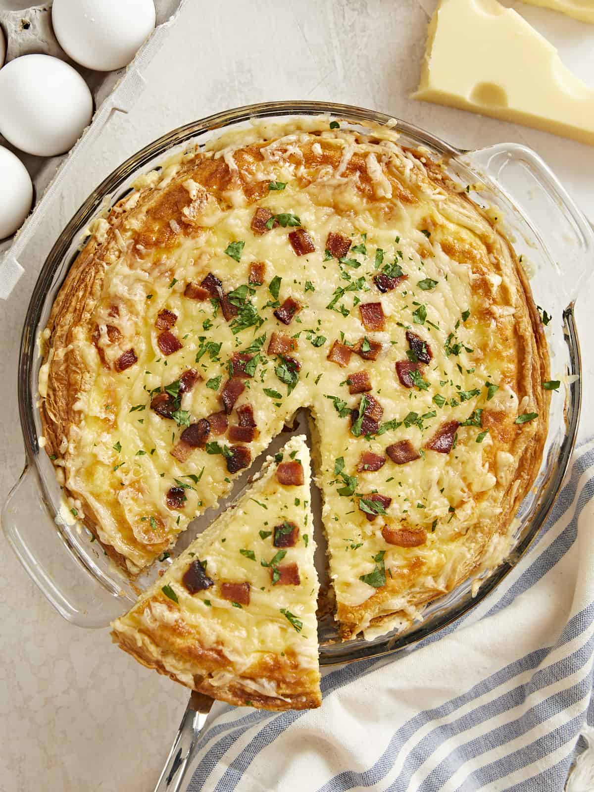 Overhead shot of a slice of Quiche Lorraine being lifted out of the pie plate.