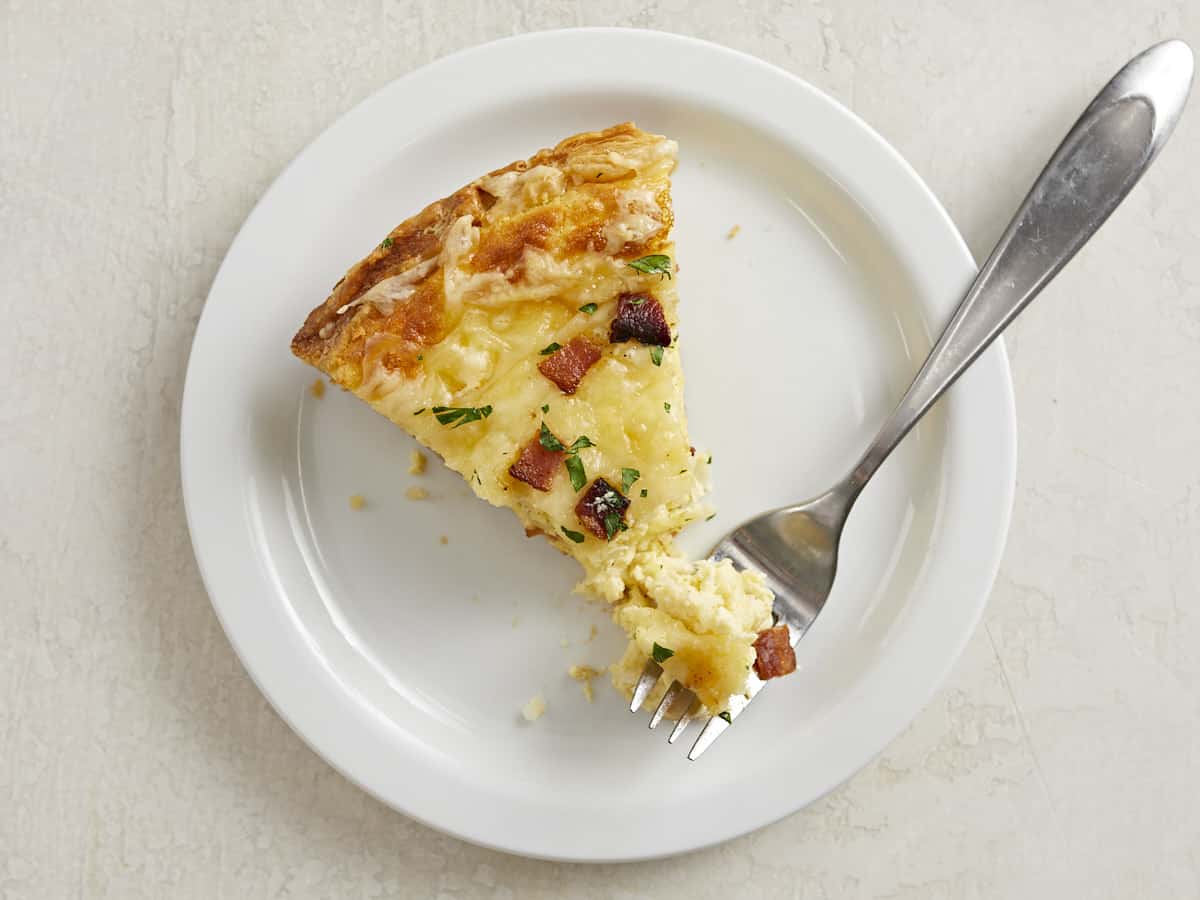 Overhead shot of a slice of Quiche Lorraine on a white plate with a fork in it.