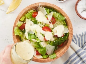 Overhead view of Caesar dressing being poured over a salad.