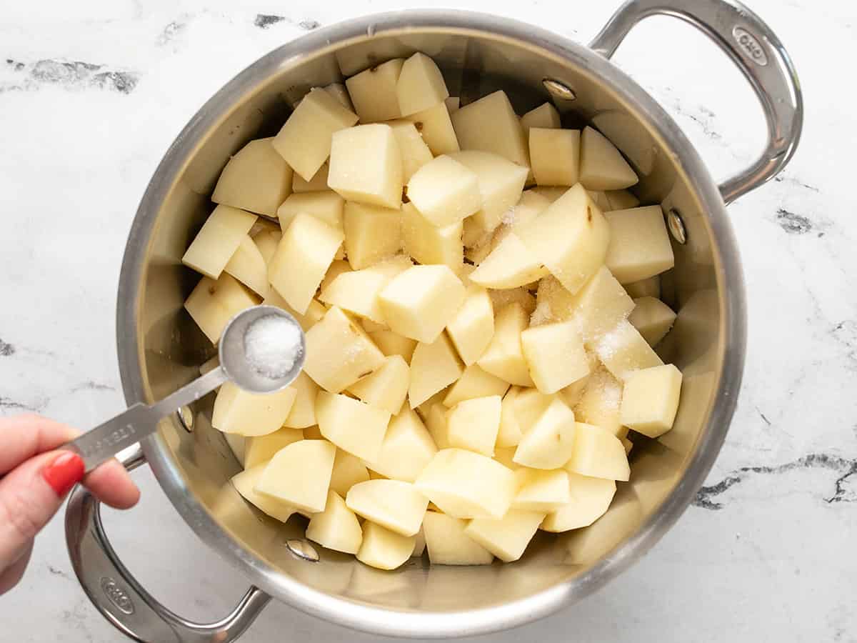 Diced potatoes in a pot with salt being sprinkled over top. 