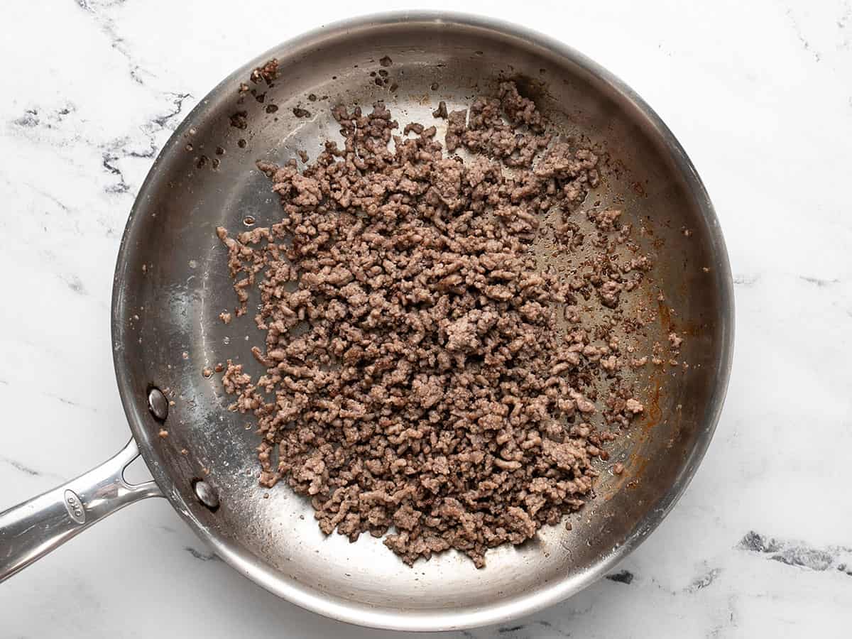 Overhead shot of ground beef browning in silver sauté pan.