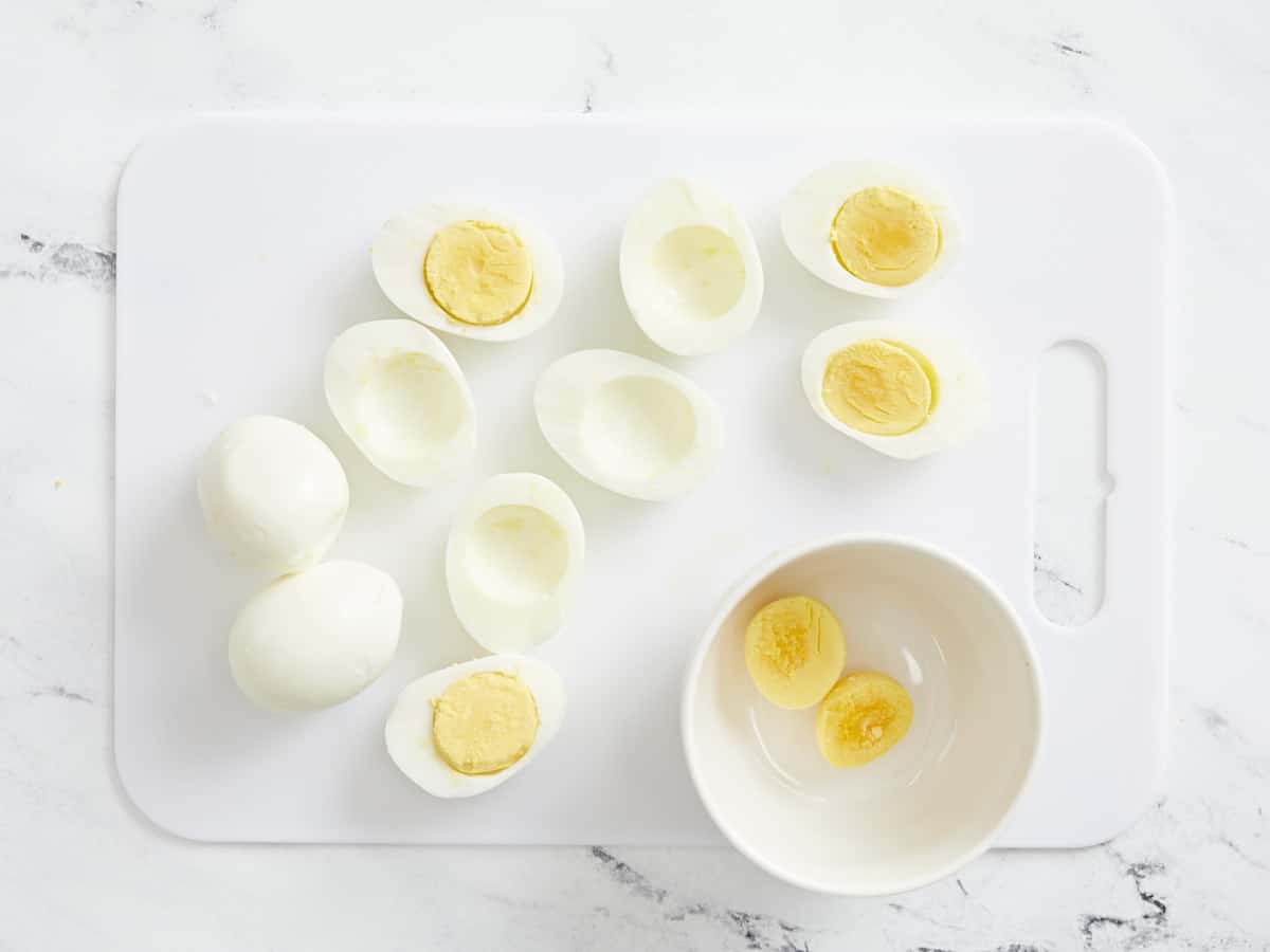 Overhead shot of hard boiled eggs, sliced in half, with yolks in a white bowl.