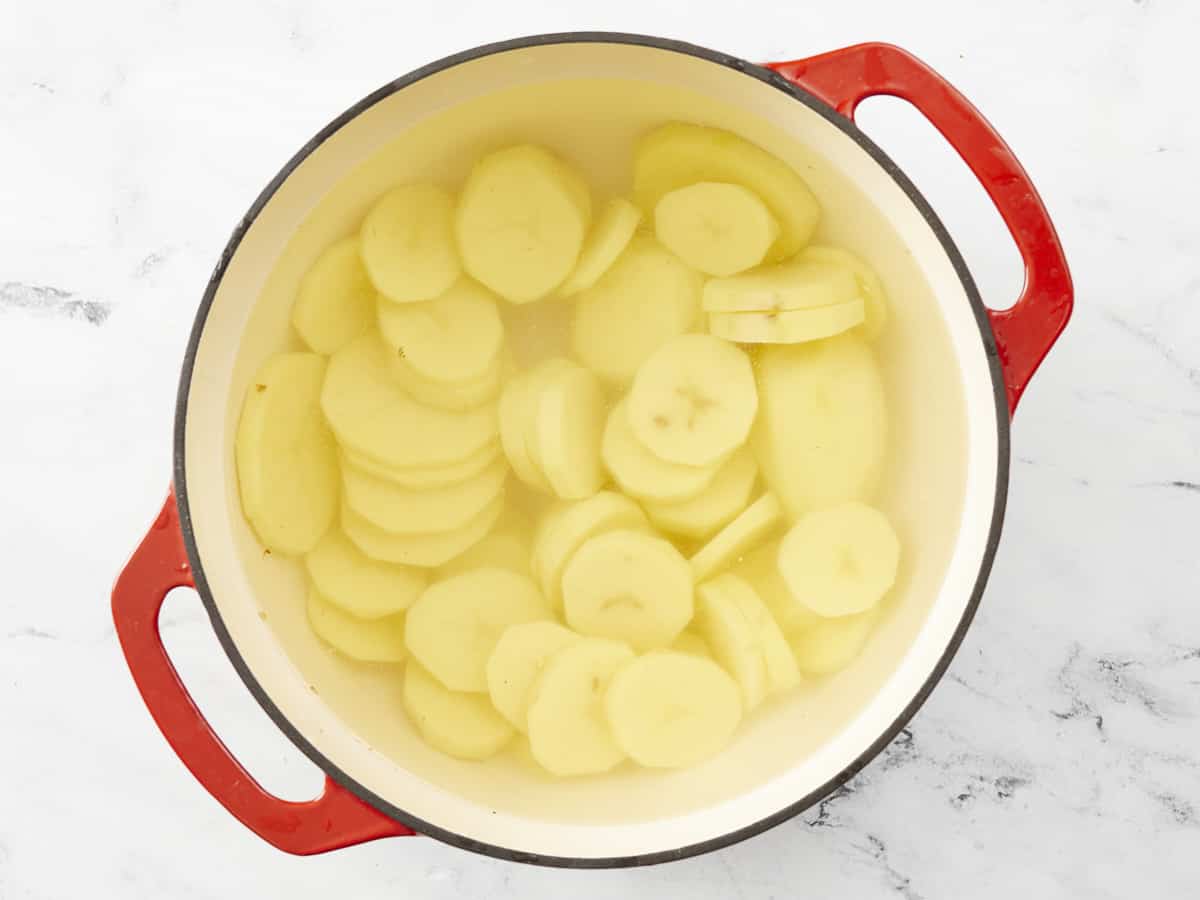 Overhead shot of a red Dutch oven with sliced potatoes in salted water.